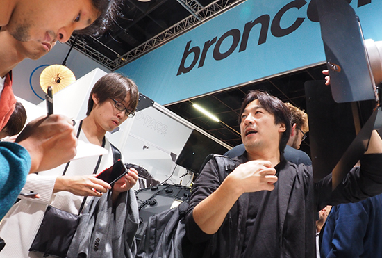 ブロンカラーブースの製品をツアー参加者に紹介するアガイ商事の吉田氏（右）